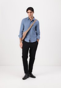 Camisa de botón azul claro hecha de algodón, pantalones negros, botas negras hasta el tobillo y un bolso color marrón claro con correas ajustables.