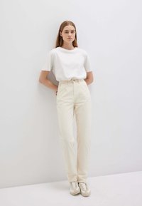 Pantaloni a vita alta in corduroy color crema con tessuto testurizzato, abbinati a una maglietta bianca a maniche corte e sneakers beige.