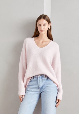 Light pink, loose-fitting, knitted sweater with a V-neck and dropped shoulders, paired with high-waisted, light blue jeans.