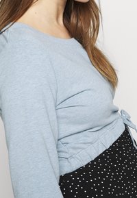 Světle modrý dlouhý rukáv top s kulatým výstřihem a staženým pasem, spárovaný s černou sukní s puntíky, která má elastický pas.