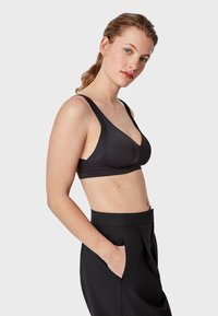 Soutien-gorge sans fil noir avec bretelles larges réglables, un design sans coutures et un tissu doux, associé à un pantalon noir taille haute.