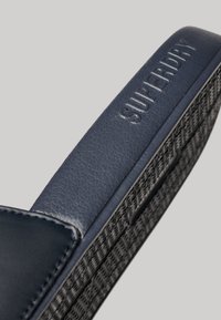 Marineblå sandal med tekstureret syntetisk overdel og mønstret gummisål. Har prægede "Superdry" logo på remmen.