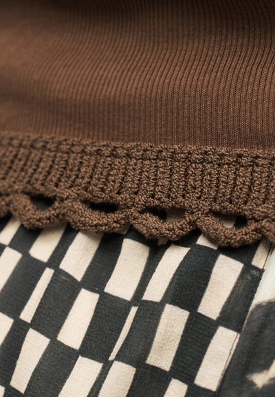 Καφέ πλεκτό ύφασμα με κυματιστό άκρο πάνω από υφάσματα με ασπρόμαυρο καρό μοτίβο.