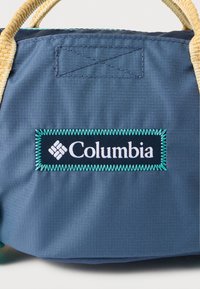 Τσάντα από ύφασμα σε χρώμα Columbia blue με μπεζ υφαντές λαβές. Διαθέτει μαύρο λογότυπο με περίγραμμα σε τυρκουάζ ραφή. Ανθεκτικός, δομημένος σχεδιασμός.