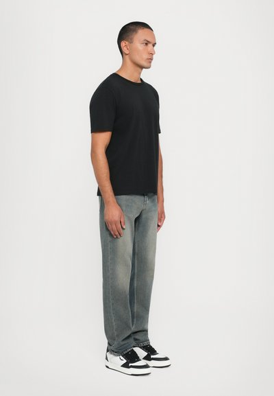 Svart kortermet t-skjorte brukt sammen med falmede blåjeans og svart-hvite joggesko. Enkelt design med en avslappet passform.