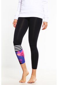 Černé legíny se zdobeným designem v barvách block, s modrým a růžovým abstraktním vzorem na dolní části nohy, zvýrazněné bílými pruhy.