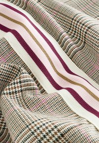 Tissu avec un motif pied-de-poule marron et noir, des rayures en tricot rose et beige, montrant la texture et les plis sur une surface de matériau douce.