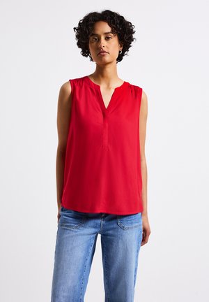 Blouse sans manches rouge avec un décolleté en V, en tissu doux, plis subtils aux épaules et coupe décontractée, portée avec un jean bleu clair.