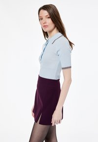 Hellblaues geripptes Poloshirt mit kurzen Ärmeln und drei Knöpfen, kombiniert mit einem dunkelvioletten Minirock mit einem Seitenschlitz.