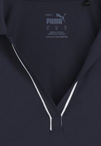 Polo de color azul marino con escote en forma de V, con ribetes blancos, hecho de una tela suave. Etiqueta con información de cuidado impresa en gris.