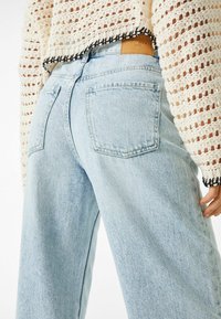 Ljusblå högmidjade jeans med en avslappnad passform, med bakfickor och en brun läderflik. Stickad topp med öppen väv och svart kant.