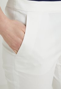 Hand inserted into the front pocket of white pants, highlighting pocket design and fabric texture.
