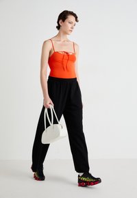 Red fitted tank top with spaghetti straps, black elastic waist trousers, and black sneakers with red and green accents, complemented by a white handbag.