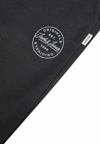 Black cotton cloth with a round white logo stating "Jack & Jones Originals Est. 1990." Small label with "Jack & Jones" at the edge.