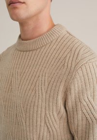 Beige kötött pulóver bordázott textúrával és finom hullámmintázattal, magas, kerek nyakkivágással. Puha, közepes súlyú anyag.