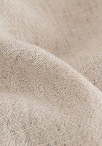 Lichtbeige stof met een gestructureerde weving, met subtiele verhoogde patronen en een zachte, licht onregelmatige oppervlakte.