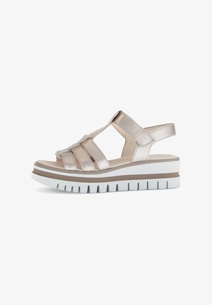 Metallic guld sandal med strappy design, en tykk hvid sål og subtile brune accenter. Har åben hæl og teksturerede stropper.