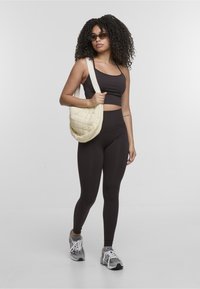 Juoda sportinė liemenėlė ir leggingai, derinami su pūstiniu kreminės spalvos petine krepšiu. Apranga pasižymi pritaikytu dizainu ir tekstūruotu audiniu. Pilki sportbačiai užbaigia įvaizdį.