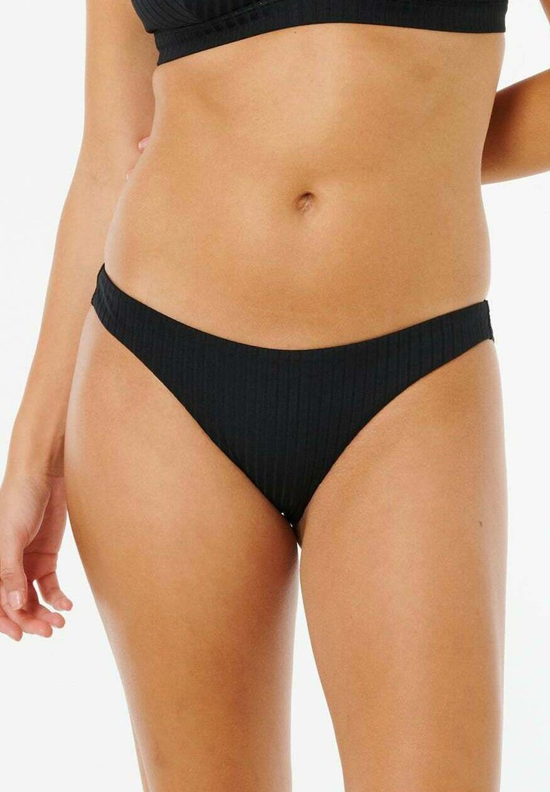 Kobieta w czarnych prążkowanych spodniach od bikini i dopasowanym topie, ukazująca środkową część ciała i biodra na białym tle.