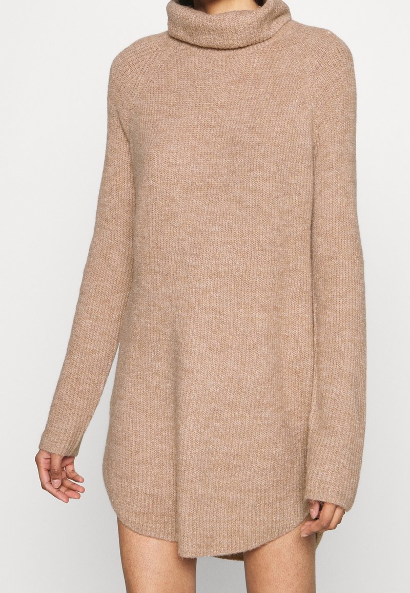 Pull en tricot beige avec un col montant, des manches longues et une coupe légèrement oversize, doté d'un tissu texturé et doux, avec un ourlet arrondi.