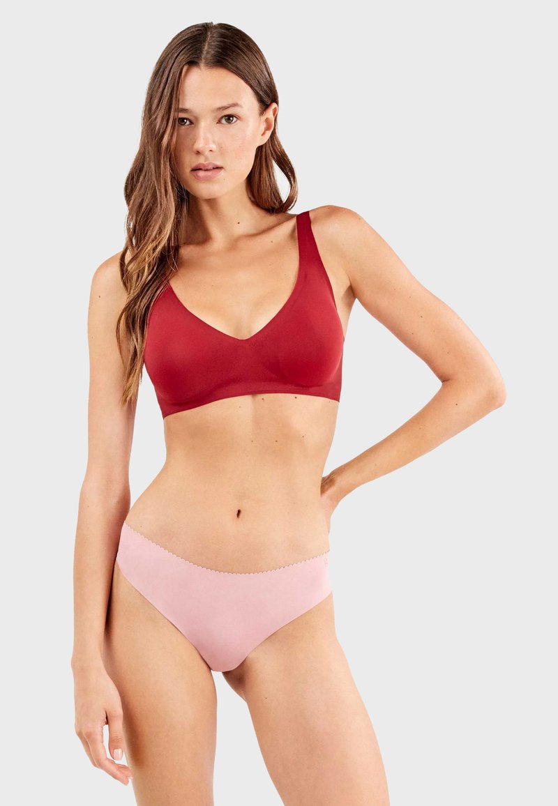 Sujetador rojo con diseño de escote en V, tirantes anchos y acabado sin costuras. Braguitas rosas con una textura suave y cinturilla con ondas.