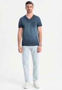 Námořnické tričko s v-neck výstřihem a kapsou, v kombinaci s světle modrými džíny a bílými teniskami. Hladký povrch s mírně vybledlým designem.