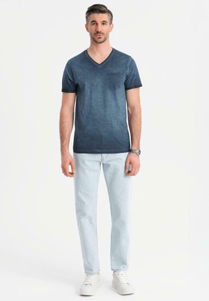 Camiseta de pico en color navy con un bolsillo, combinada con jeans de un tono azul claro y zapatillas blancas. Textura suave con un diseño ligeramente desgastado.