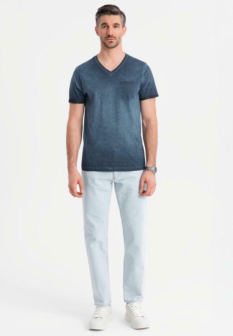 Námořnické tričko s v-neck výstřihem a kapsou, v kombinaci s světle modrými džíny a bílými teniskami. Hladký povrch s mírně vybledlým designem.
