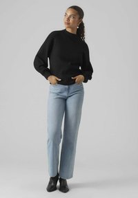 Maglione nero a maniche lunghe con collo alto, abbinato a jeans a gamba dritta blu chiaro e stivali neri alla caviglia. Tessuto liscio, vestibilità moderna.