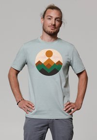 Lichtblauwe t-shirt met korte mouwen met een cirkelvormige bergafbeelding in oranje en groen. Zachte stof met een ronde hals.