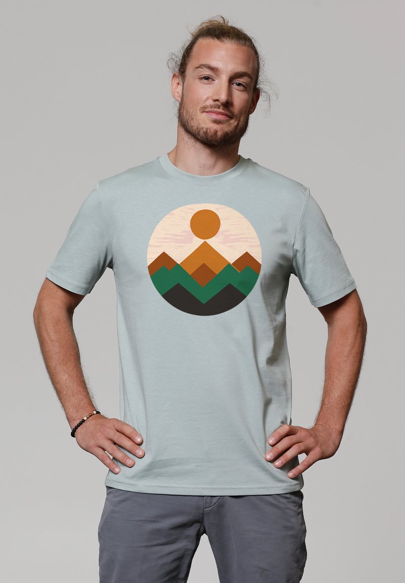 Lichtblauwe t-shirt met korte mouwen met een cirkelvormige bergafbeelding in oranje en groen. Zachte stof met een ronde hals.