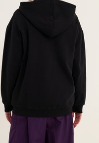 Felpa con cappuccio nera realizzata in tessuto morbido, dotata di una vestibilità rilassata, polsini a coste e un design semplice e privo di adornamenti.