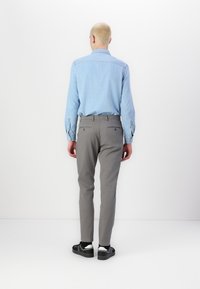 Světlomodrá denimová košile s knoflíkovými manžetami a šedé kalhoty s úzkým střihem. Černobílé tenisky dokončují oděv, pohled zezadu.