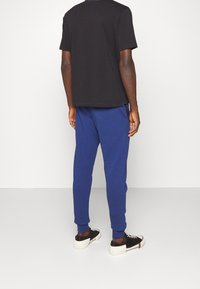 Black cotton t-shirt with short sleeves, paired with blue jogger pants and black sneakers. Simple design, relaxed fit, and ribbed cuffs.