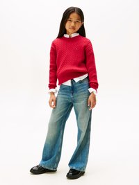 Rød kabelstrikket genser over en hvit skjorte med krage, kombinert med vide blå denimjeans og svarte sko, med en avslappet passform.