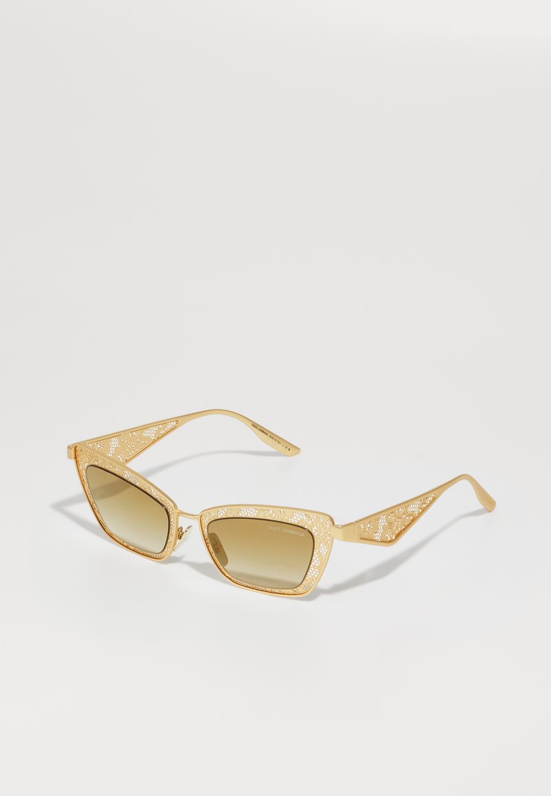 Gold metal sunglasses with a geometric cat-eye shape, featuring intricate cut-out designs on the temples and brown gradient lenses.