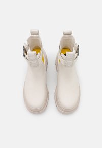 Bottes blanches à la cheville en cuir lisse avec une bride texturée, un intérieur jaune et une semelle en caoutchouc épaisse pour l'adhérence et la durabilité.