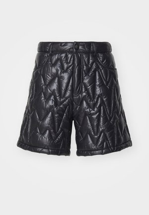 Shorts noirs en tissu matelassé et brillant. Dotés d'une fermeture éclair, de poches avant et d'un motif de surpiqûre en zigzag sur la surface.