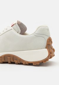 Bílé semišové tenisky s texturovanou gumovou podrážkou, zaobleného tvaru, s béžovými akcenty a malým logem značky na patě.