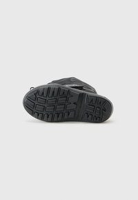 Svart sneaker med teksturert såle og synlig logo, plassert på en ren hvit bakgrunn. Fokus på skoens dekkdesign.