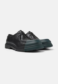Schwarze Lederschuhe mit abgerundetem Zehenbereich, grünem Gummikappen an der Zehe und strukturiertem Außensohle. Schnürdesign mit dezenten Nähten.
