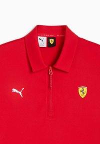 Polo rouge en tissu lisse, doté d'un col à demi-fermeture éclair, avec le logo Puma blanc et l'emblème Ferrari sur la poitrine.
