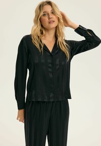 Czarny satynowy zestaw piżamowy składający się z koszuli na guziki z długim rękawem i pionowymi paskami oraz spodni z elastycznym pasem, oba z miękką fakturą.