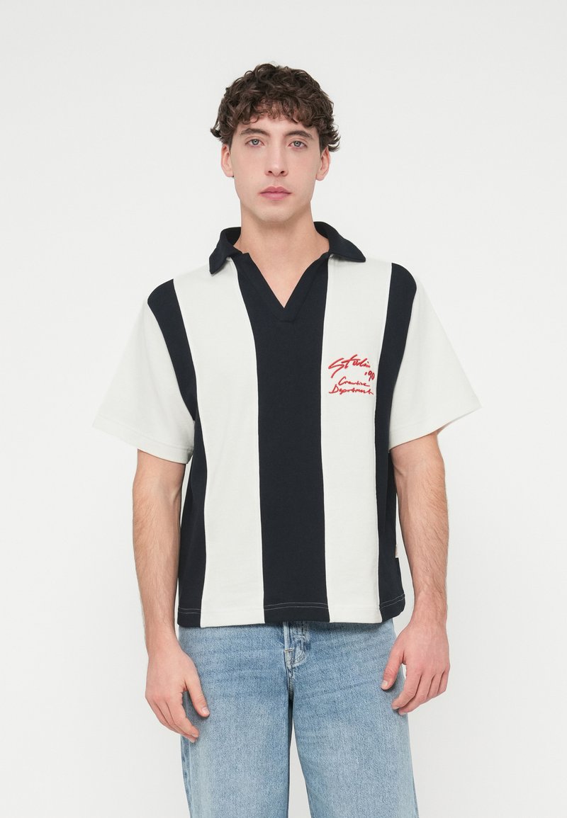 Κοντομάνικο πόλο μπλουζάκι με V-λαιμόκοψη, με κάθετες ναυτικές και λευκές ρίγες και κόκκινο κεντητό κείμενο στο στήθος.