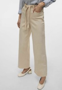 Beiga vida byxor med hög midja, med ett knytbälte och sidofickor, tillverkade av ett mjukt denimmaterial.