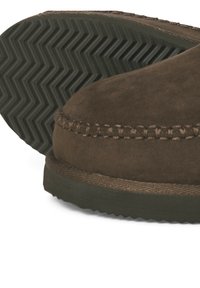 Chaussure slip-on en daim marron avec un détail cousu le long du col et une semelle en caoutchouc texturée présentant un motif en zigzag.