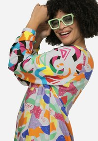 Bunt gemustertes Kleid mit abstrakten Formen in mehreren Farben. Lange Ärmel mit unterschiedlichen Designs und einem weichen, strukturierten Stoff.