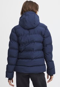 Námornícka modrá prešívaná bunda s kapucňou, s prešitým prešívaným dizajnom a elastickými manžetami. Tkanina vyzerá hladko a ľahko.