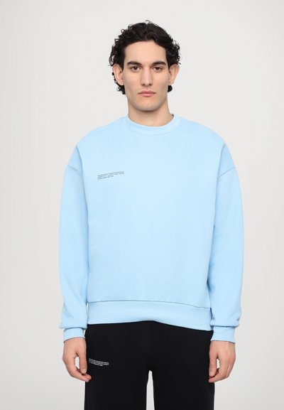 Lyseblå bomulds sweatshirt med rund hals og sænkede skuldre. Har minimal sort tekst på forsiden og ribbede manchetter ved ærmerne.