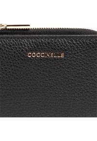 Portefeuille en cuir noir texturé avec le logo doré "Coccinelle", doté d'une fermeture zippée et de coutures visibles. Design compact adapté aux indispensables.